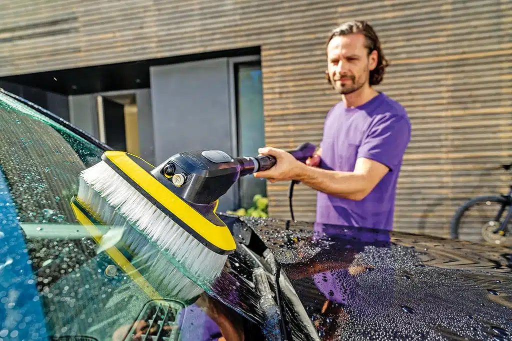 Mann reinigt die Windschutzscheibe eines Autos mit Hochdruckreiniger mit Waschbürstenaufsatz